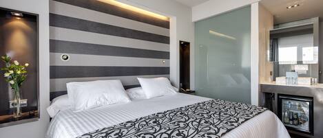 A modern hotel room with a large bed, a built-in mini-fridge, and a stylish striped wall design.