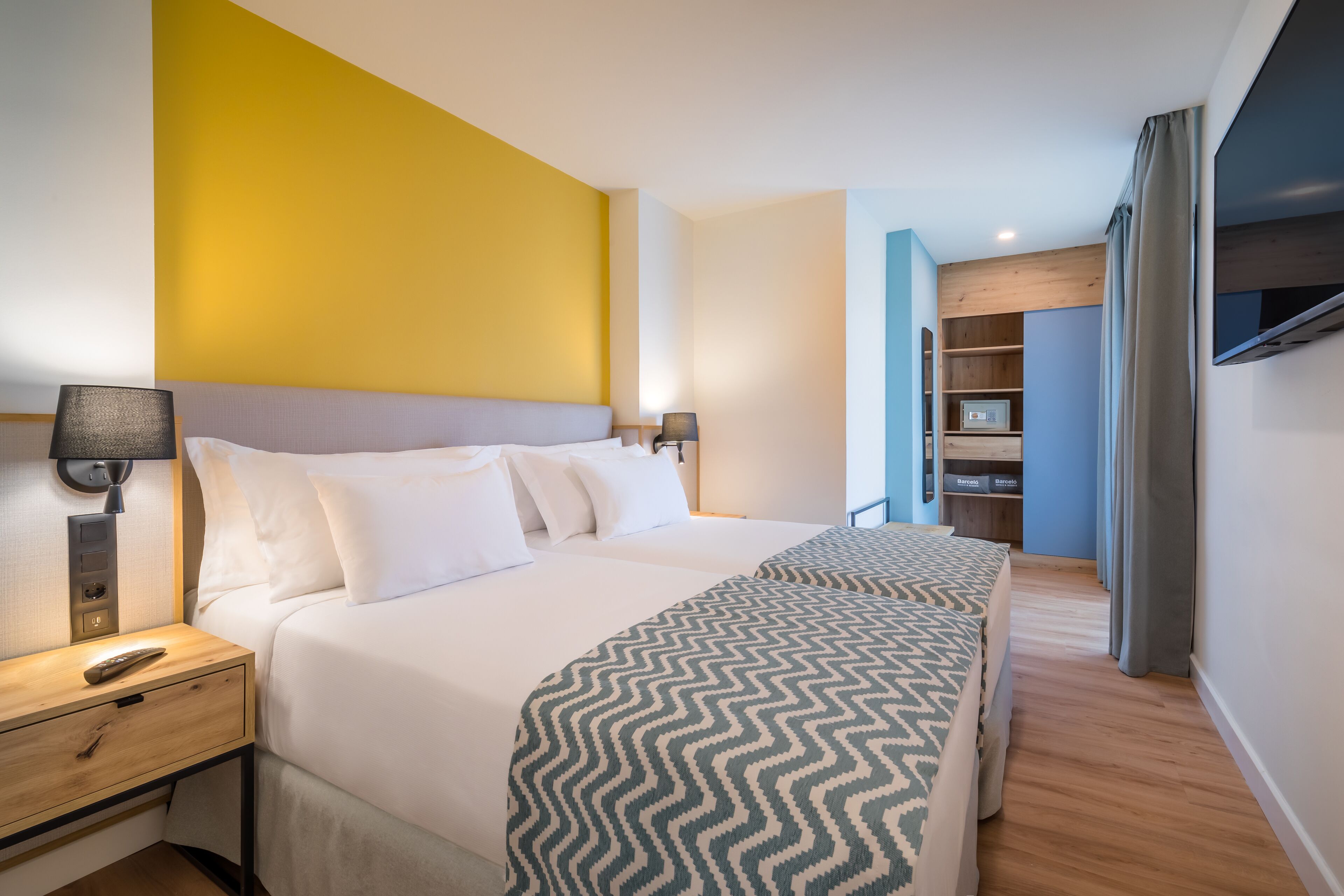 Una habitación de hotel con una cama grande, lámparas de noche, un televisor y un armario.
