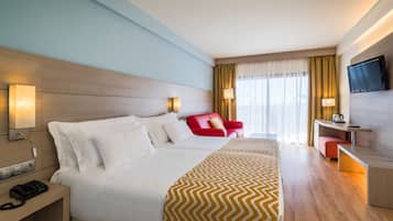 Una habitación de hotel con una cama grande, un escritorio con silla, un televisor montado en la pared y una ventana con cortinas.