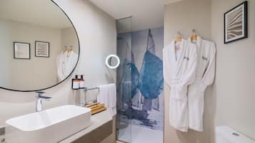 A modern bathroom with a freestanding bathtub, a glass shower enclosure, and two white robes hanging on a rack.