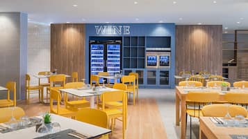 A modern restaurant with yellow chairs and tables, a wine display, and a blue wall with the word "WINE".