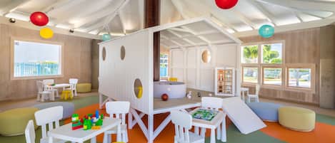 Una sala de juegos infantil con muebles blancos, alfombras de juego coloridas y un amplio ventanal con vistas al exterior.