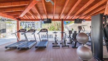 Une salle de sport couverte équipée de tapis de course, de vélos elliptiques et de ballons d’exercice.
