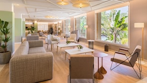 Un vestíbulo de hotel amplio, bien iluminado, con mobiliario moderno, ventanas grandes que ofrecen vistas a zonas verdes y un diseño limpio y contemporáneo.