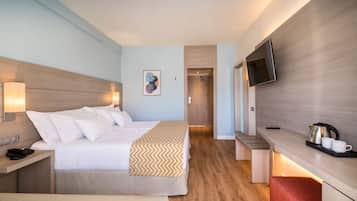 A hotel room with a bed, bedside table, lamp, TV, and a small kitchenette area.
