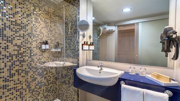 Un baño con pared de ducha de mosaico, un lavamanos con encimera azul, un espejo, un secador de pelo y un perchero para toallas.