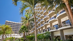 Un hotel con varios balcones, palmeras y un cielo azul despejado.