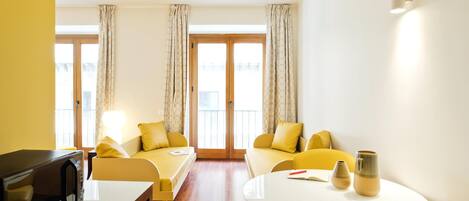 A modern hotel room with a sofa set, a dining table, and a microwave.