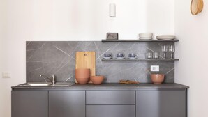 Una cocina moderna con armarios grises, salpicadero de mármol, tabla de cortar de madera y una repisa con cuencos y vasos.