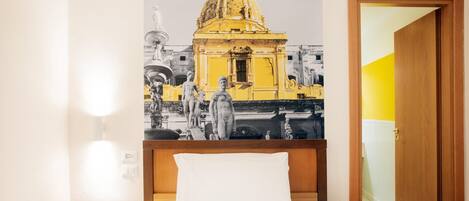 Una habitación de hotel con una cama, una mesita de noche, una lámpara de pared y una puerta.