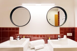 Un bagno con due lavandini, uno specchio e pareti rivestite di piastrelle rosse.