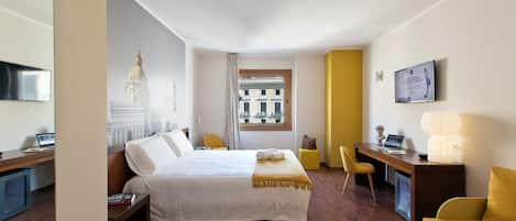 A modern hotel room with a large bed, a desk with a computer, a chair, and a TV mounted on the wall.