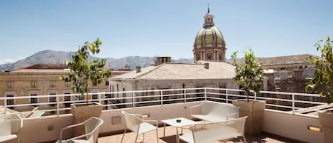Una terraza en la azotea con mobiliario exterior, vista a un edificio histórico con cúpula y montañas al fondo.
