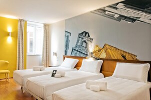 Camera d'albergo con due letti, una parete gialla e un grande murale raffigurante un edificio.