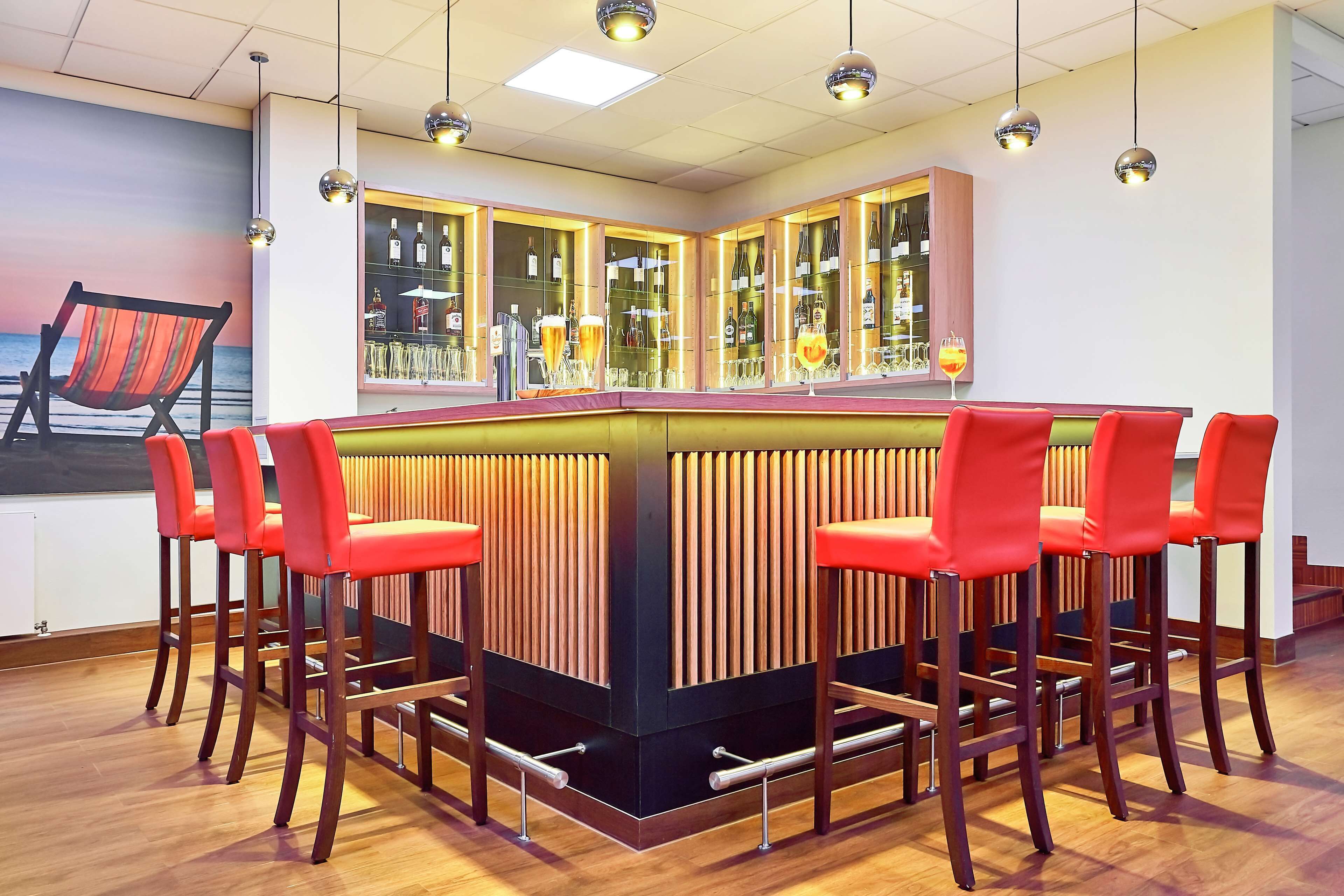 A bar area with a wooden bar counter, red bar stools, and a view of the sea through a mural.