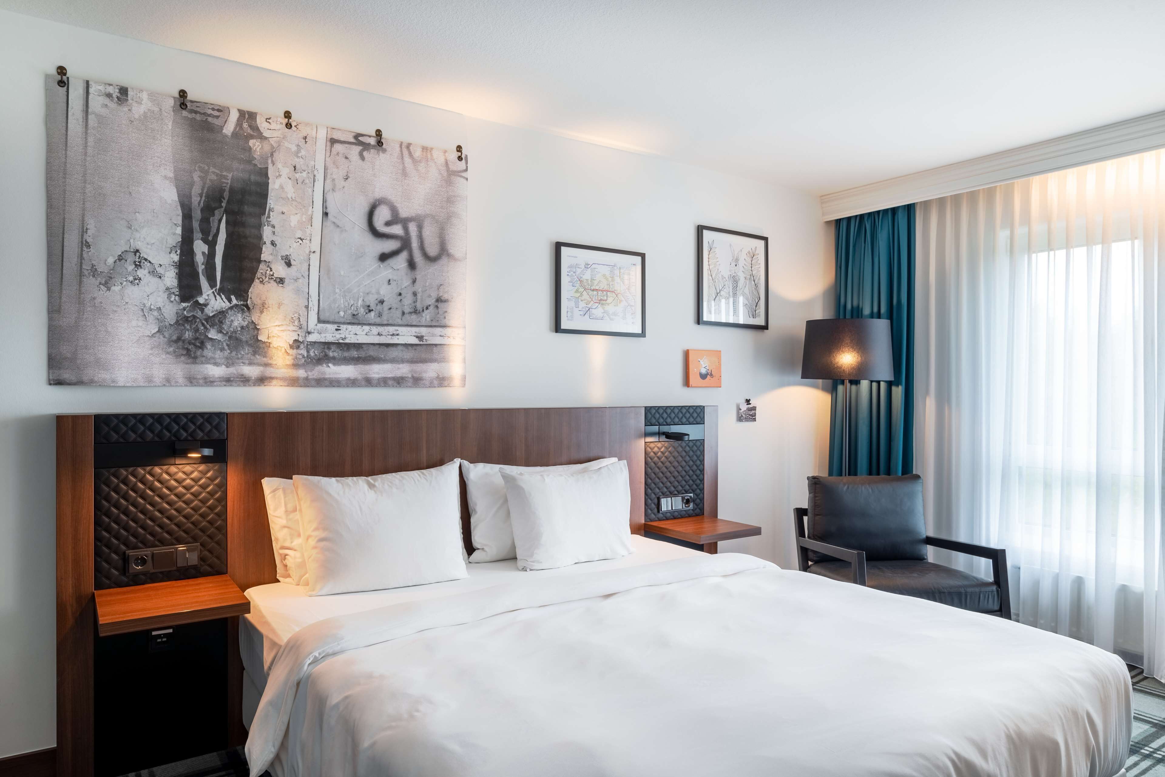 Une chambre d’hôtel avec un grand lit, une tête de lit à motifs matelassés, des tables de chevet, une lampe et des œuvres d’art accrochées au mur.