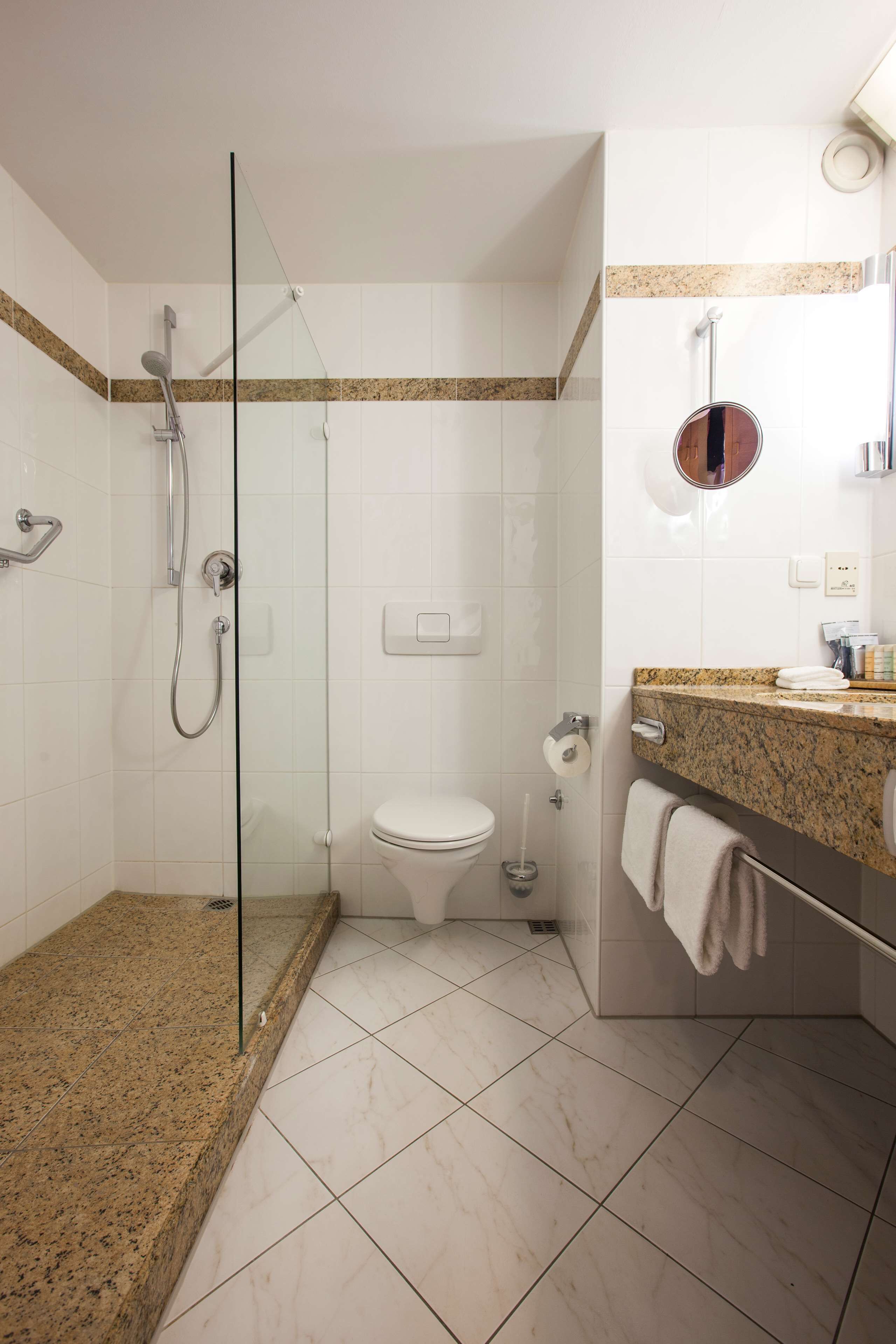 A modern bathroom with a glass-enclosed shower, a toilet, and a granite countertop with a towel hanging on the side.