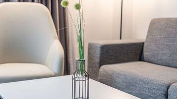 En moderne stue med et hvidt sofabord, en grå sofa, en grå lænestol, en gulvlampe og en vase med grønne planter.