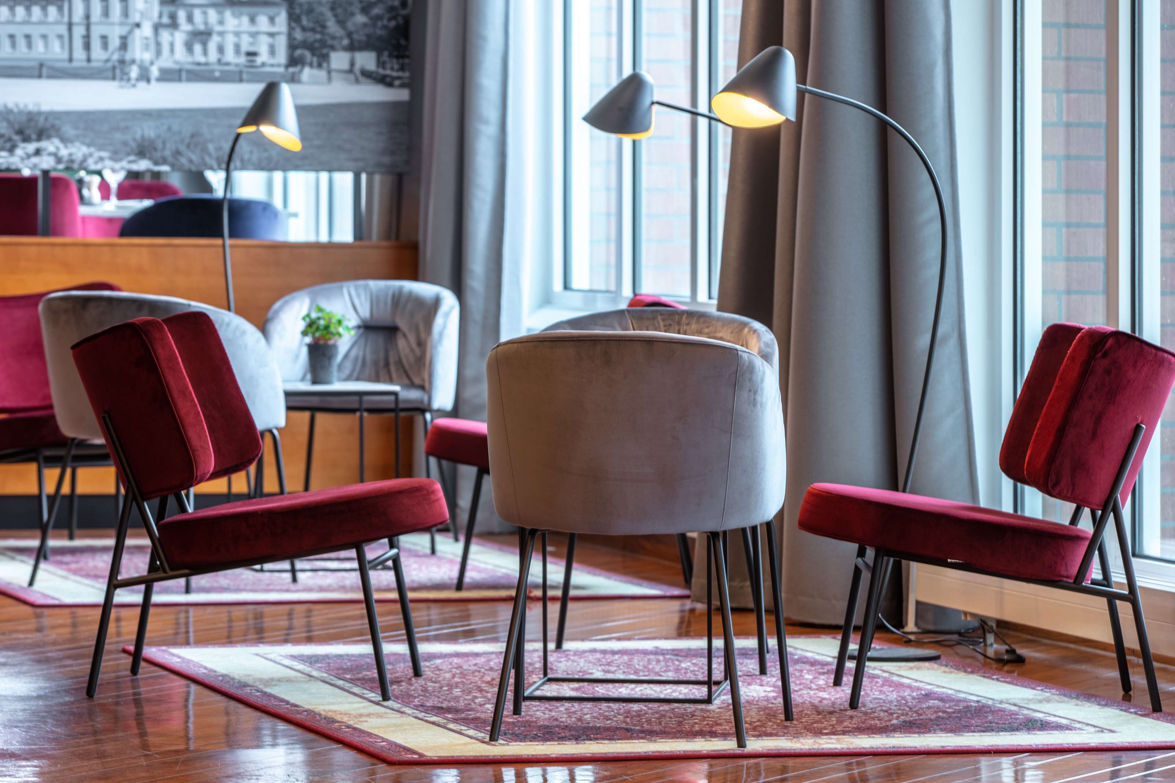 A modern interior with a seating area featuring red and grey upholstered chairs, a round table, and a floor lamp.