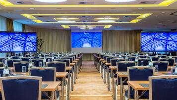 Ein Konferenzraum mit Tischen und Stühlen, großen Bildschirmen an den Wänden und einem modernen Deckengestaltungsstil.