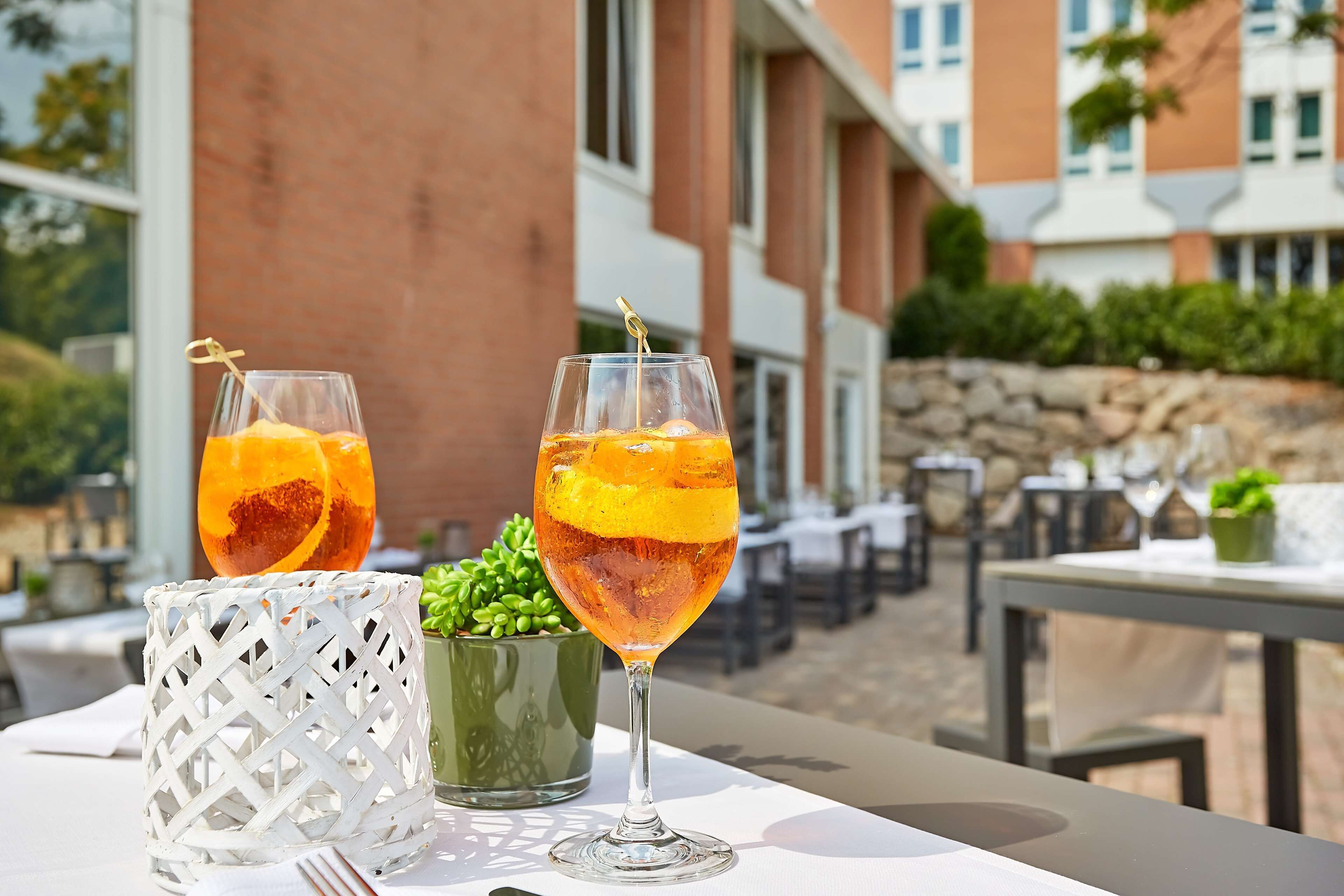 Twee glazen oranje drank op een tafel met een witte, grillige bak en een groene plant ernaast.