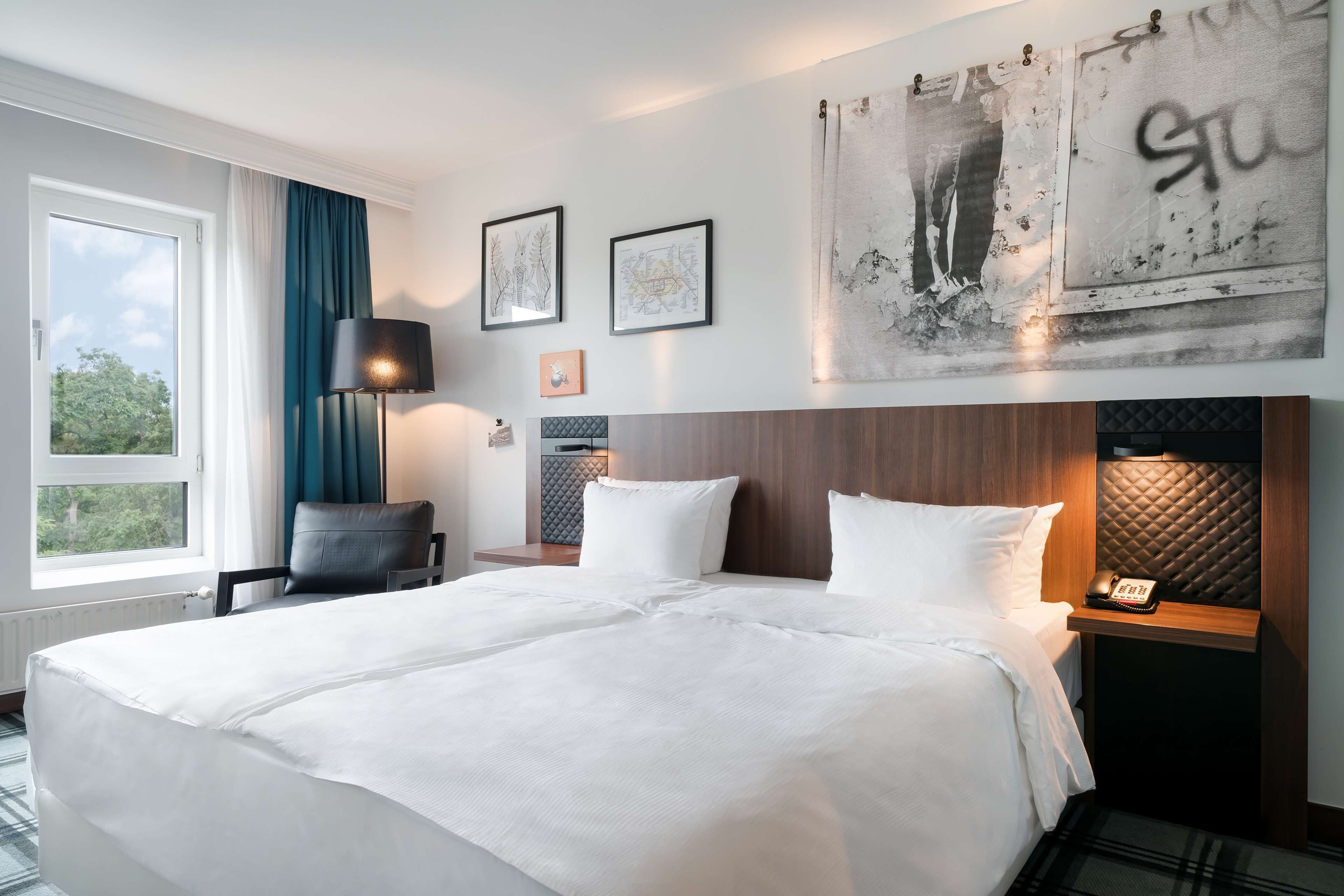 A hotel room with a large bed, a desk with a telephone, a chair, and artwork on the walls.