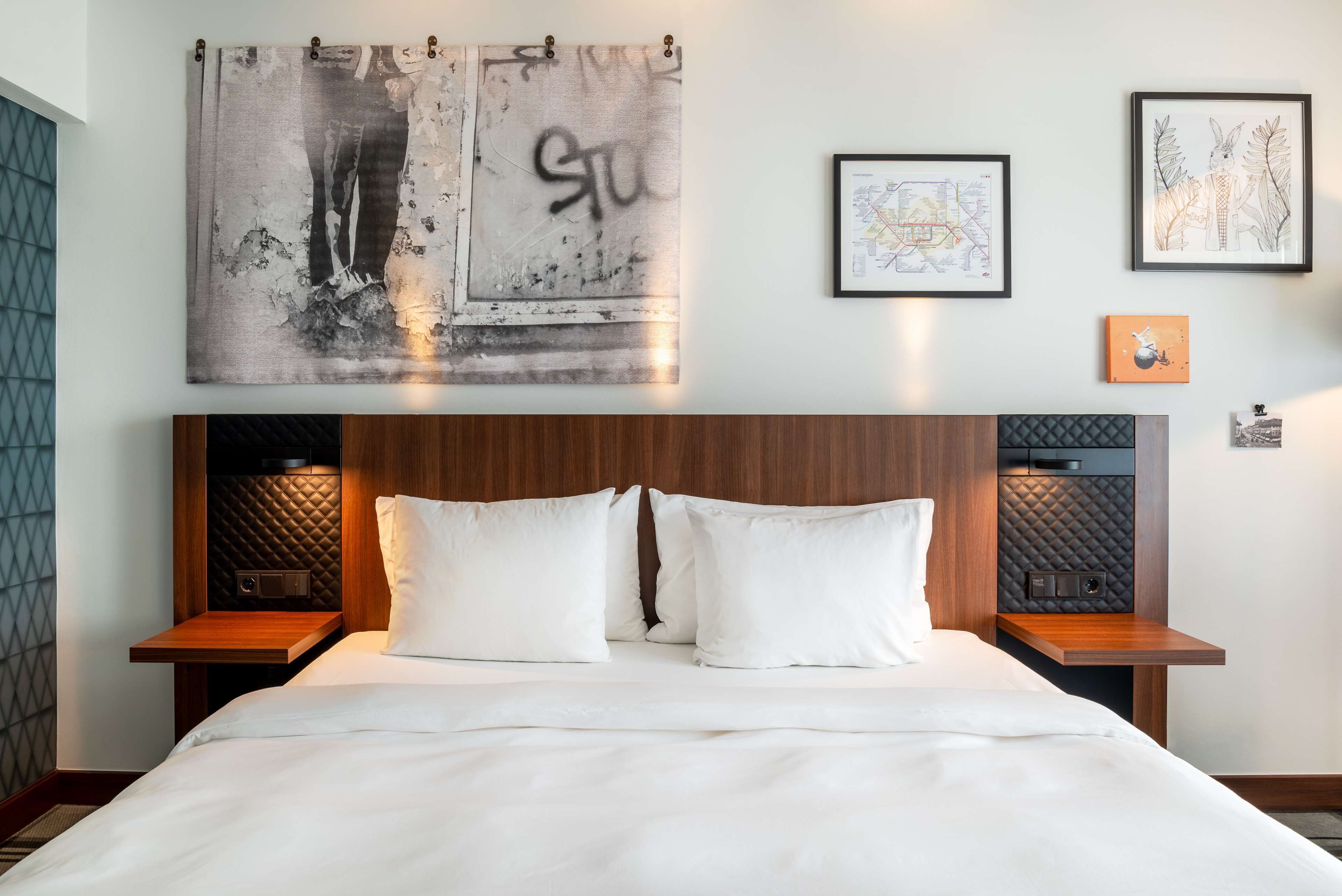 Una habitación de hotel con una cama grande, dos mesitas de noche, un cabecero con diseño acolchado y obras de arte en las paredes.