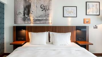 Una habitación de hotel con una cama grande, dos mesitas de noche, un cabecero con diseño acolchado y obras de arte en las paredes.