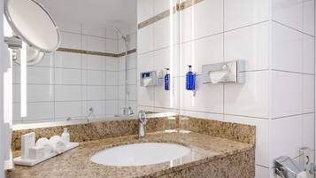A modern bathroom with a granite countertop, a white sink, a mirror, and a shower.