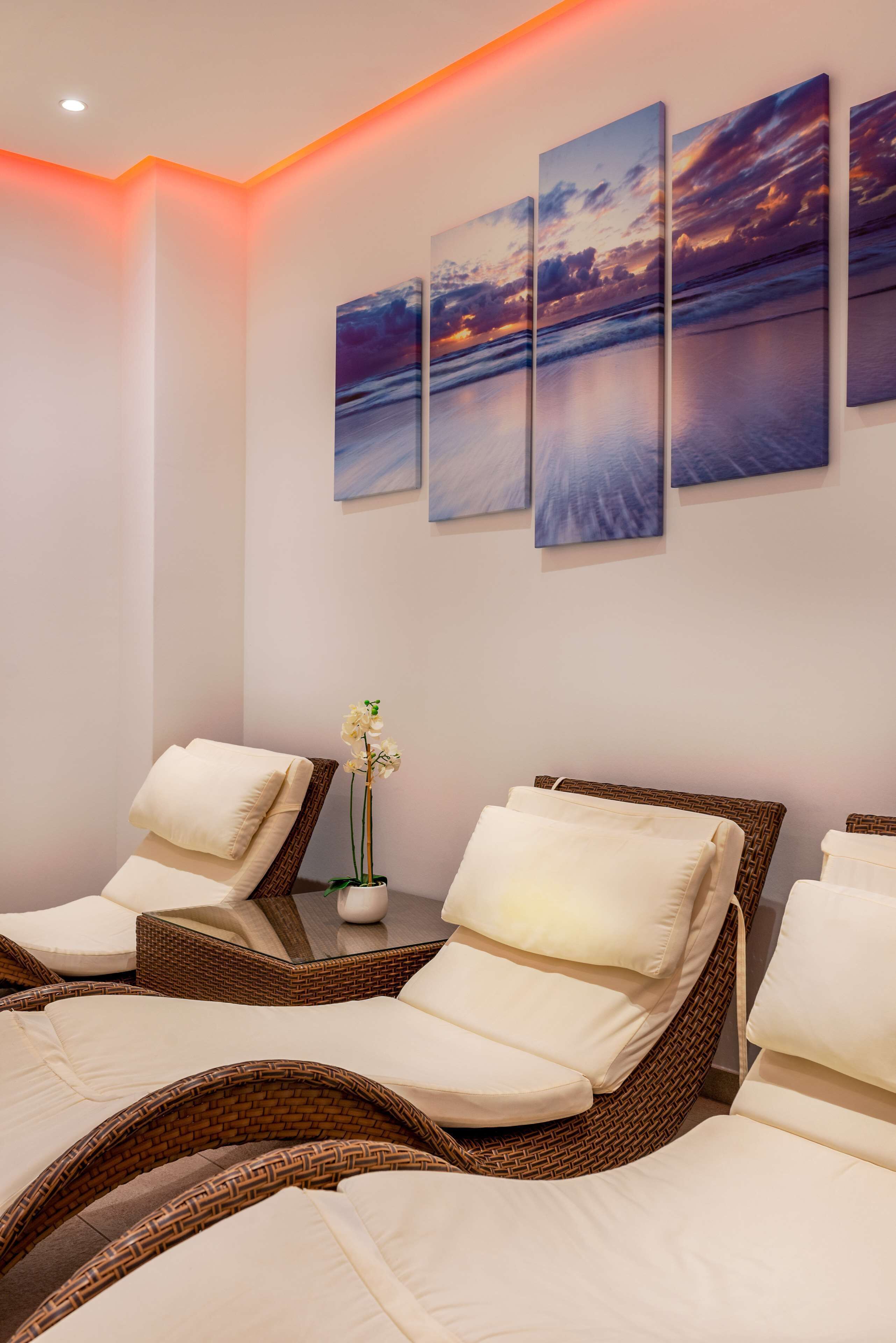 A spa room with reclining chairs, a wall-mounted painting, and a small table with a vase.