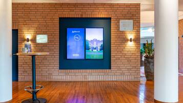 Een hal met een bakstenen muur, een digitaal scherm met Radisson Meetings branding, een kleine tafel met een fles en een potplant.
