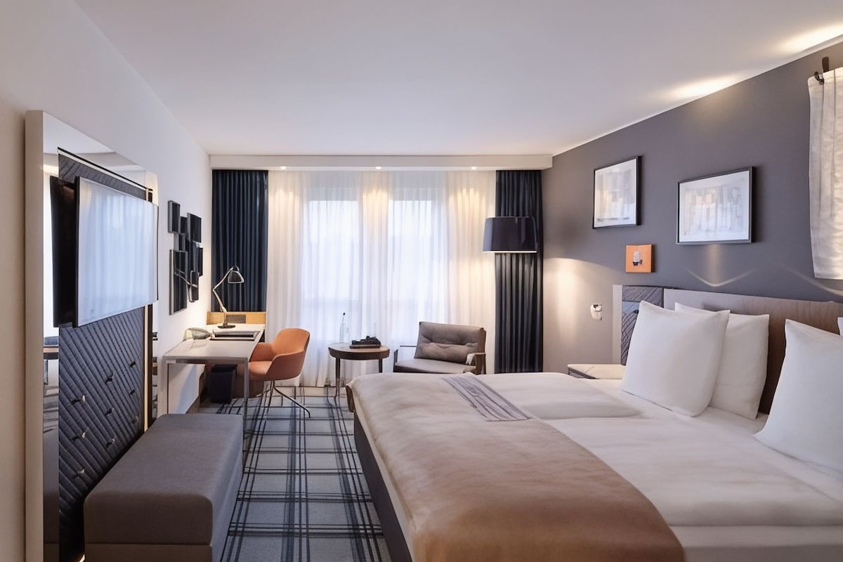 A hotel room with a large bed, a desk, a chair, and a sofa.