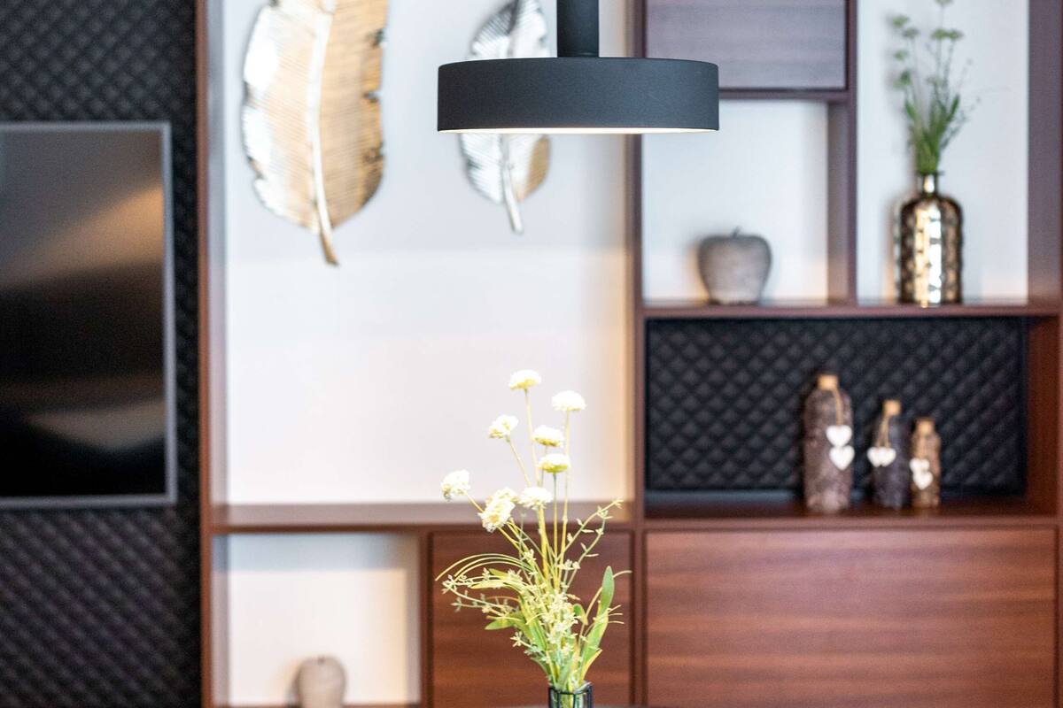Un comedor moderno con una mesa redonda de madera, una lámpara colgante negra y un florero con flores.