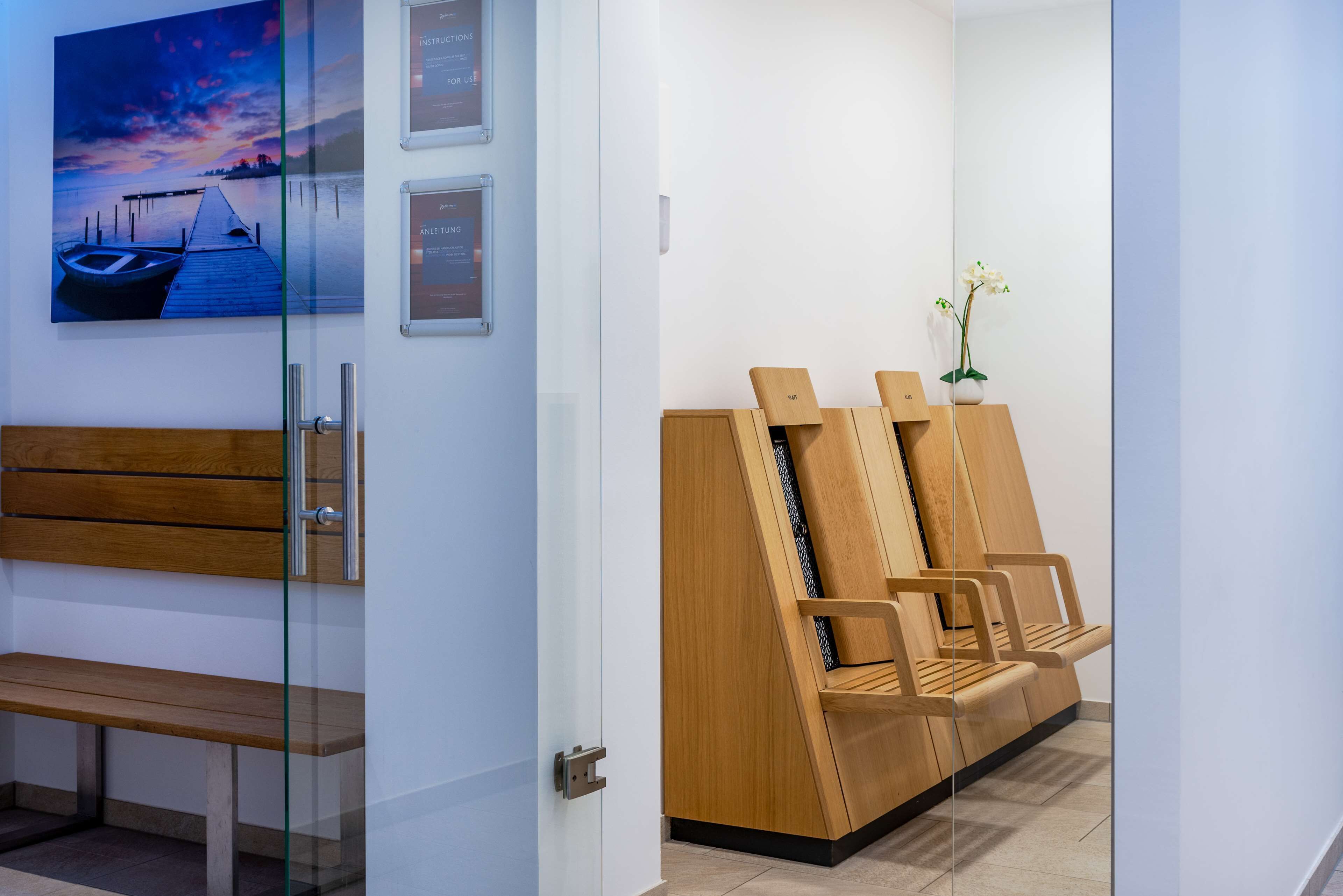 Un área de espera moderna con un banco de madera, un mostrador de recepción y una zona de estar con sillas y una planta en maceta.