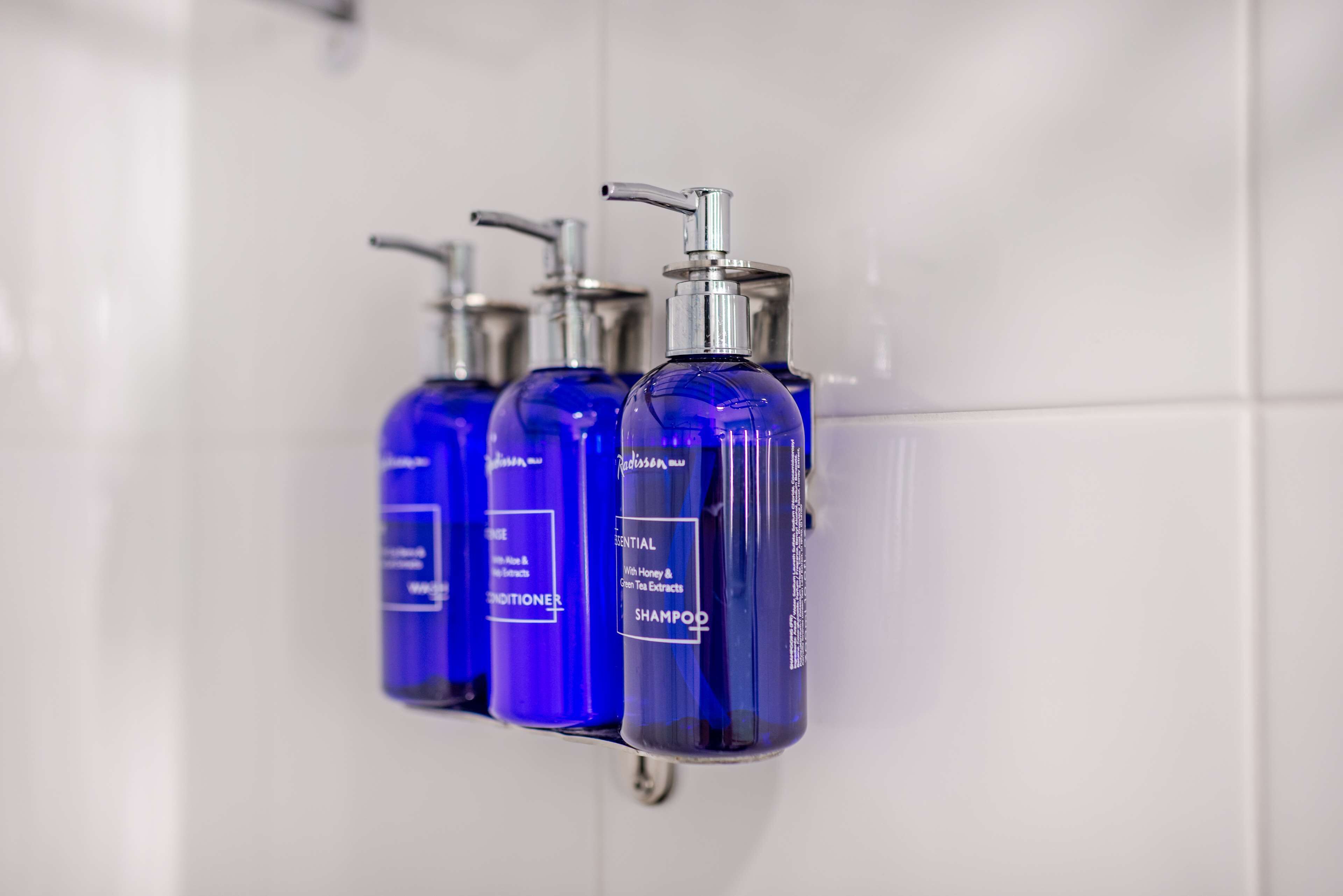 A bathroom with three blue shampoo bottles on a wall-mounted dispenser.