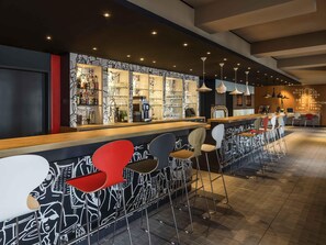 Eine Bar mit einer langen Theke, Hockern und einer Wand mit abstrakter Kunst.