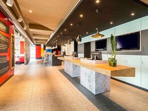 Un hall d’hôtel moderne avec un long comptoir d’accueil, un espace salon et un grand écran de télévision.