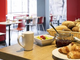 A breakfast setting with a mug, croissants, a bowl of fruit, and a basket of bread.