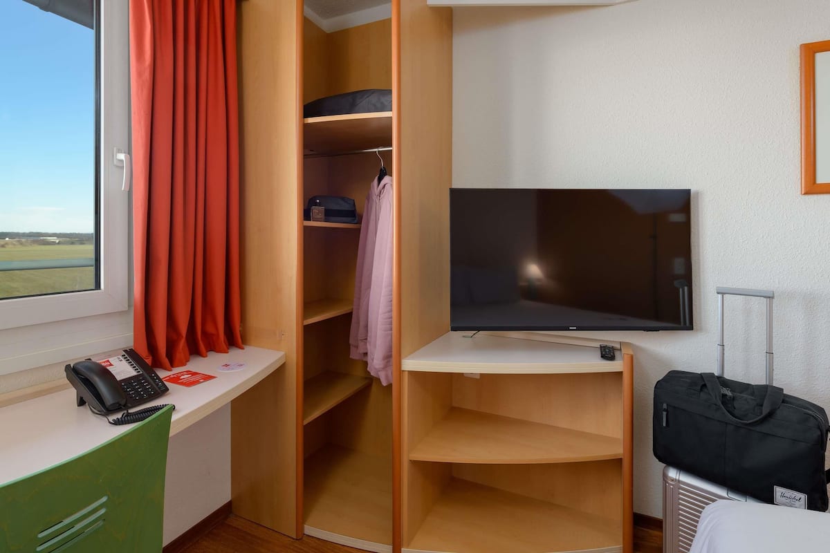 Habitación de hotel con cama, escritorio con teléfono, televisor y armario con estantes.