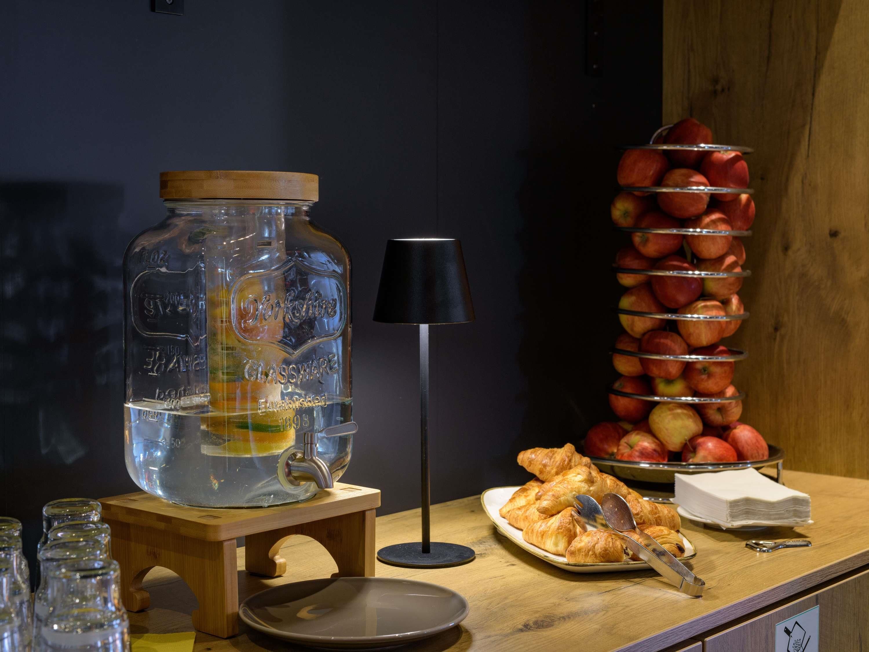 A breakfast setup with a glass jar, apples, croissants, and a lamp.