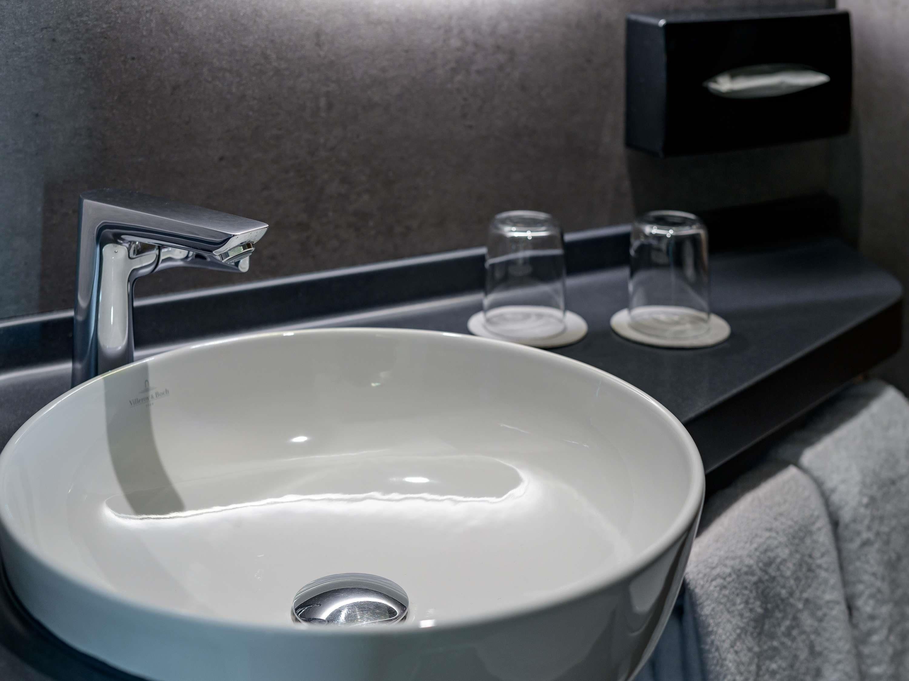 A modern bathroom with a white sink, a chrome faucet, and two clear glass soap dispensers on a dark countertop.