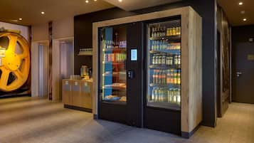 A modern hotel lobby with a large, illuminated sculpture, a self-service beverage station, and a refrigerated display case with various drinks.