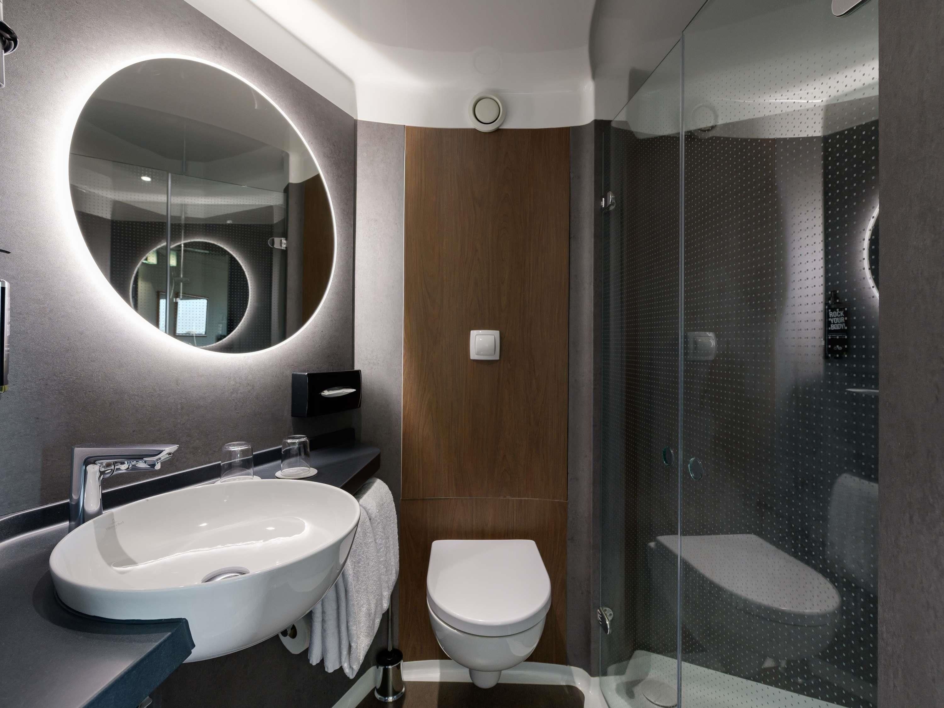 A modern bathroom with a large oval sink, a round mirror, a toilet, and a glass-enclosed shower area.
