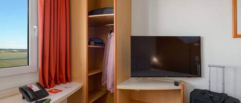 Habitación de hotel con cama, escritorio con teléfono, televisor y armario con estantes.