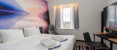 A hotel room with a bed, a desk, a chair, a TV, and a large wall mural.