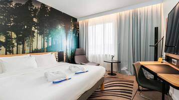 A hotel room with a bed, a desk, a chair, a small table, and a TV.