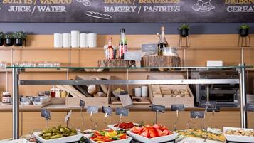 Zona de bufé con estaciones de comida señalizadas, que incluyen jugos, panadería y pastelería.