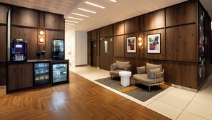 A modern lobby with wooden paneling, a seating area with a sofa and armchairs, a coffee machine, and a refrigerator. - Novotel Vilnius Centre (Vilnius)