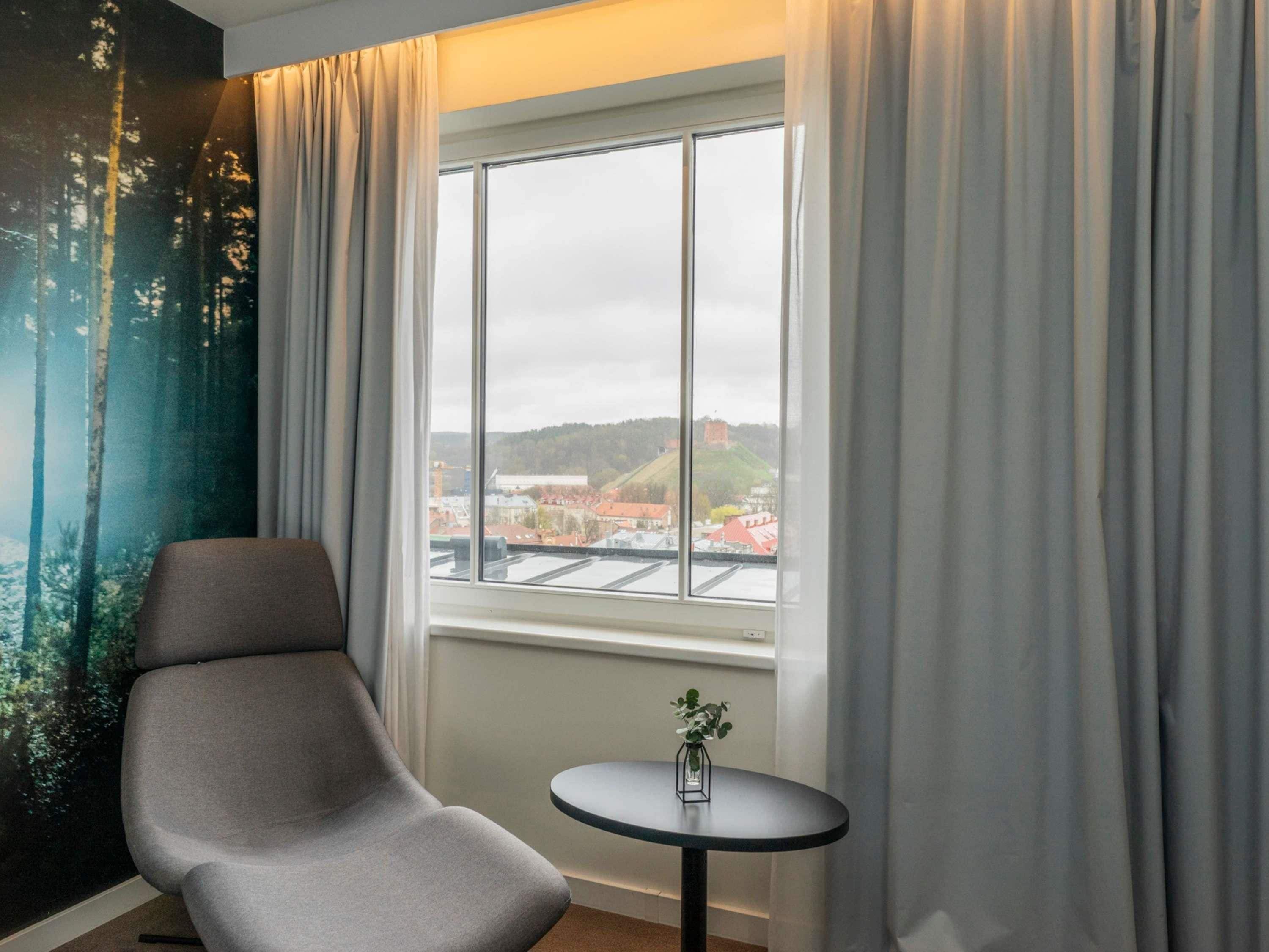 Een kamer met uitzicht op een stad, een stoel en een klein tafeltje met een vaas.