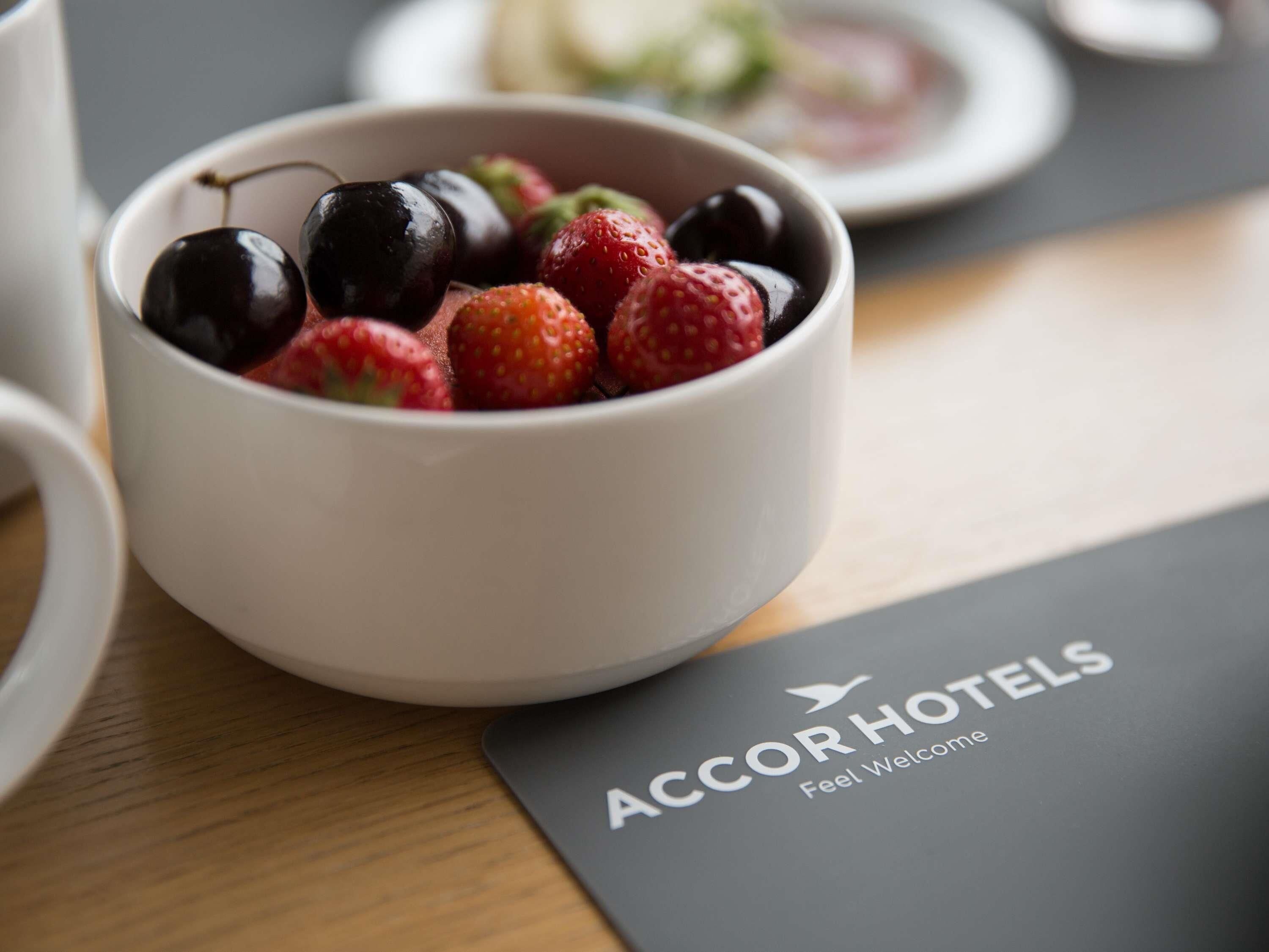 A bowl of fruit on a table with a brochure for AccorHotels.